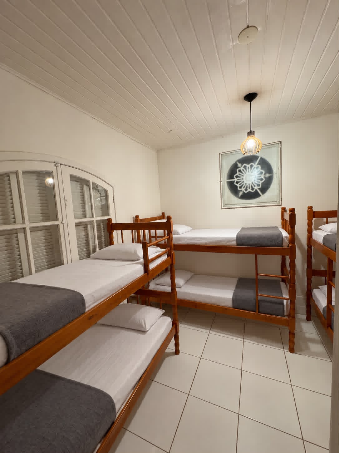 Quarto compartilhado com beliches de madeira e roupa de cama branca e cinza
